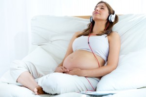 Pregnant woman sitting on sofa at home and listening music in he